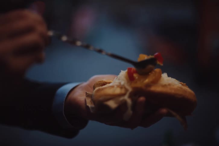 Man adds condiments to a hot dog with a long metal spoon