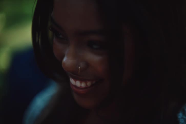 A woman with long straight hair a nose piercing and a blue shirt laughs merrily