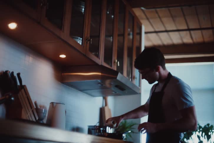Man in apron cooking and pouring oil into a frying pan