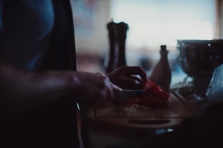 Closeup of an adult slicing a tomato on a wooden cutting board