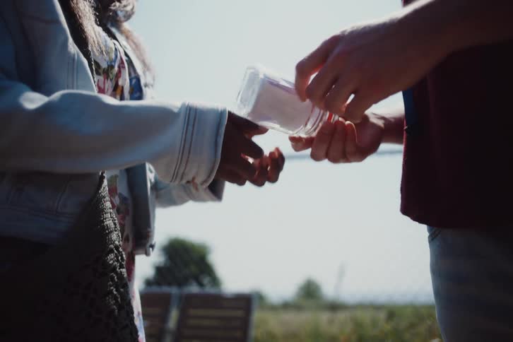 A woman gives a glass jar to a man and they exchange a hug afterwards