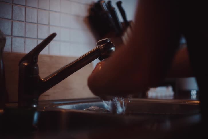 Man washing his hands in the kitchen sink and drying them with a towel