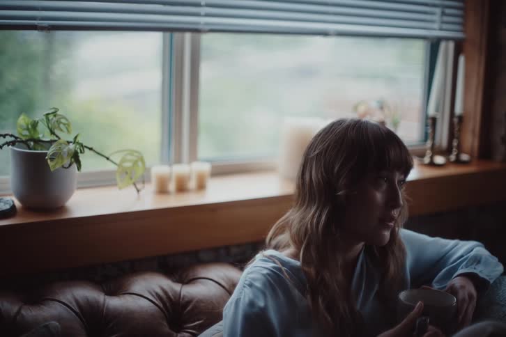A woman sits on a couch drinking from a mug
