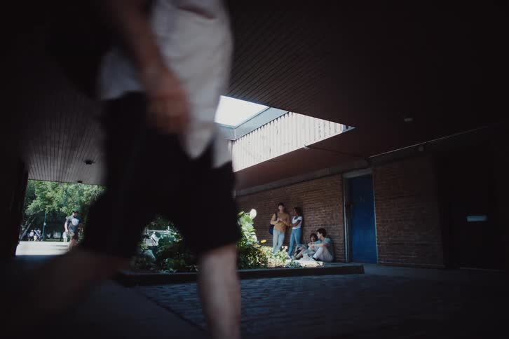 A small group of friends hang out next to their school while other people walk by