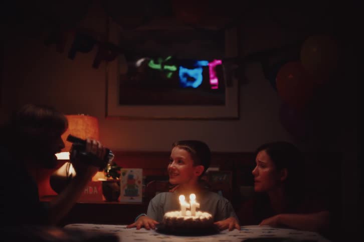 A joyful moment of a young boy celebrating his birthday with a cake lit by candles and an adult likely his mother leaning in close while the room is warmly lit and decorated