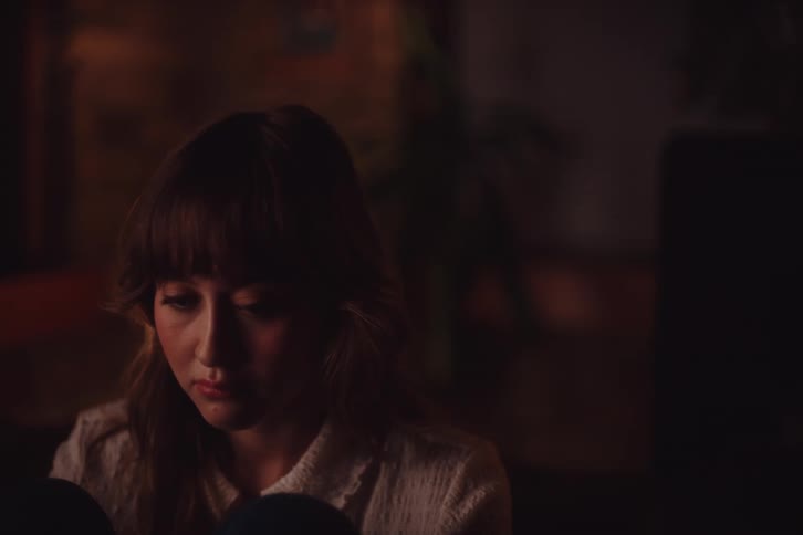 Woman sitting in a dimly lit room with a sad facial expression