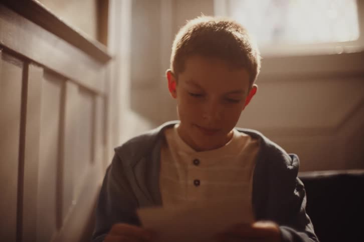 The boy reads a letter and checks photos while sitting on the stairs