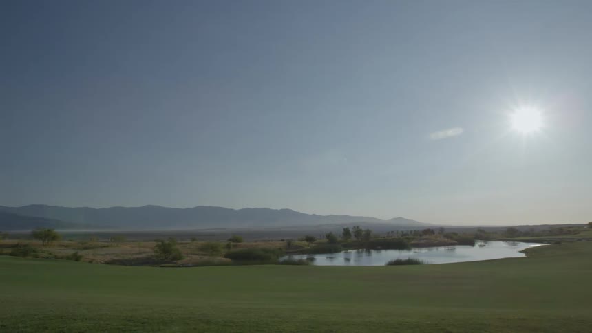 Small lake sitting in the middle of a green field on a clear day