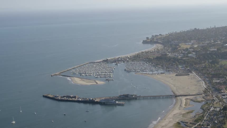 A long pier juts into a harbor off a beach on a sunny day