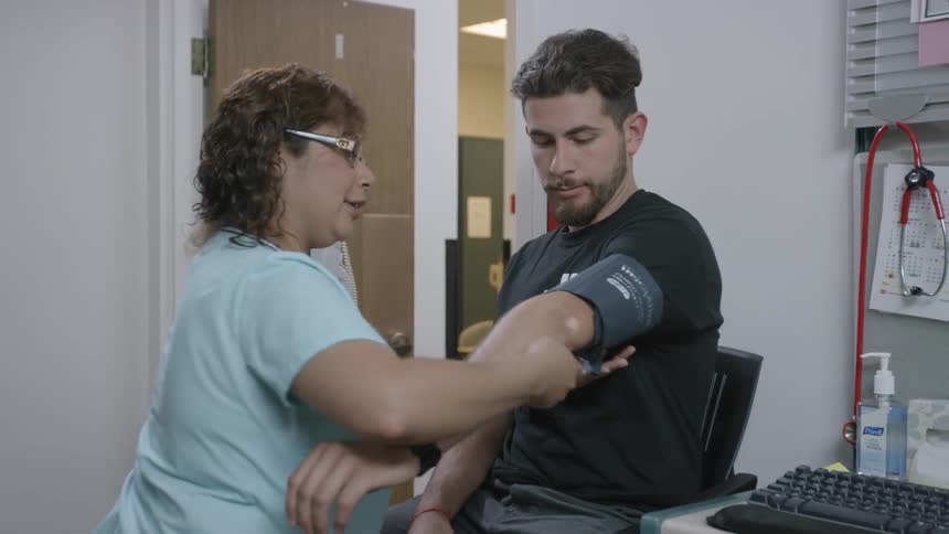 A nurse is taking a man's blood pressure in an exam room