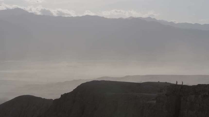 Two people walk near the edge of a large canyon during the day