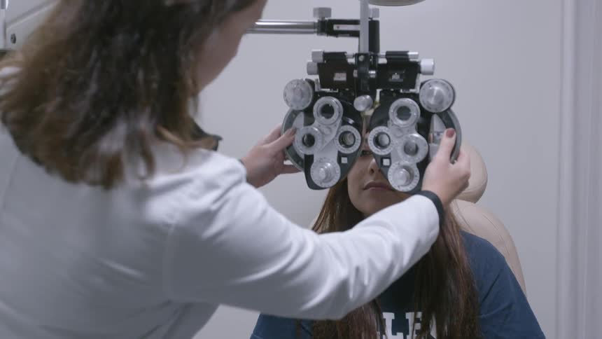 An optometrist is placing a phoropter in front of a woman's face