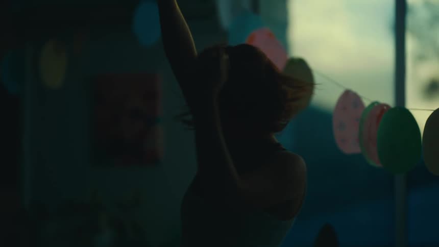 A female dancer with flowing red hair wearing a white shirt dances gracefully in dim light