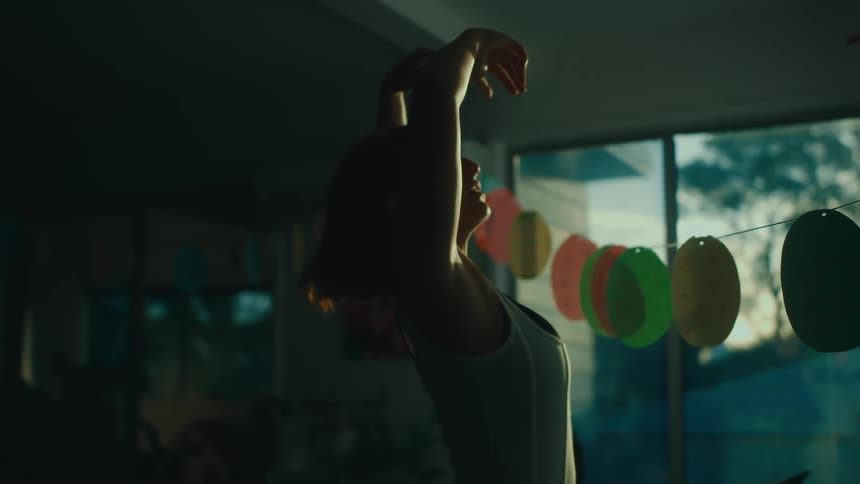 A female dancer with red hair eyes closed and arms raised dances gracefully in dim light conveying a serene and introspective mood