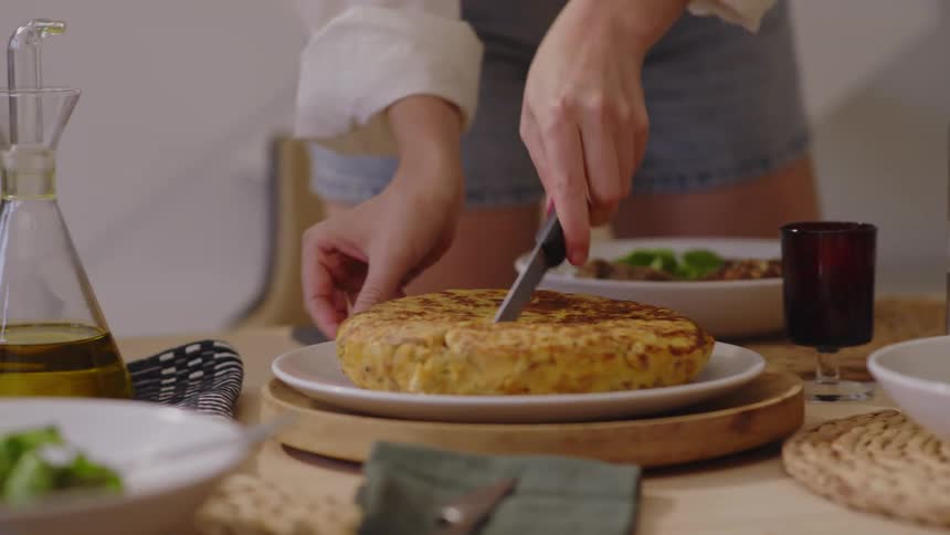 Woman stands at the dinner table and slices into food