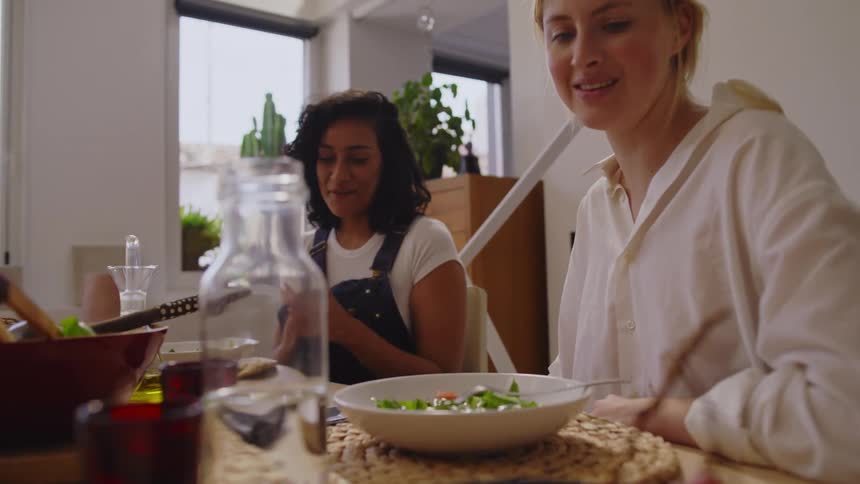 Two women sitting at a table with vegetables and fruits talking and eating
