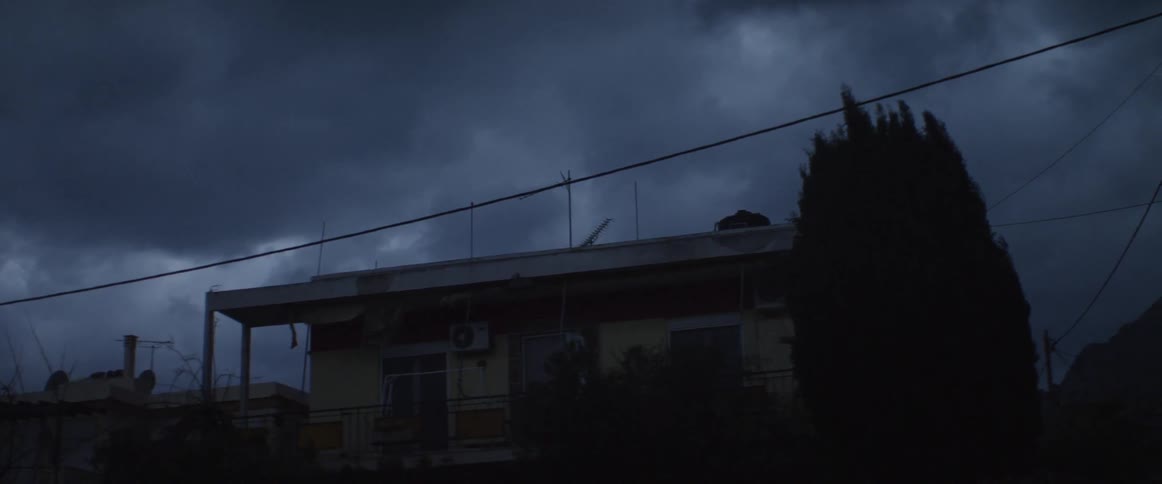 View of a home with dark clouds and wind moving trees