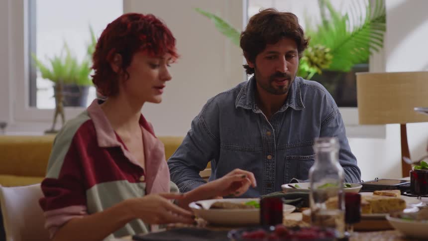 Man and woman sitting at a table serving themselves and chatting happily