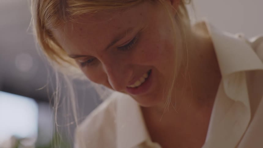 A young blonde woman smiles while slicing a quiche