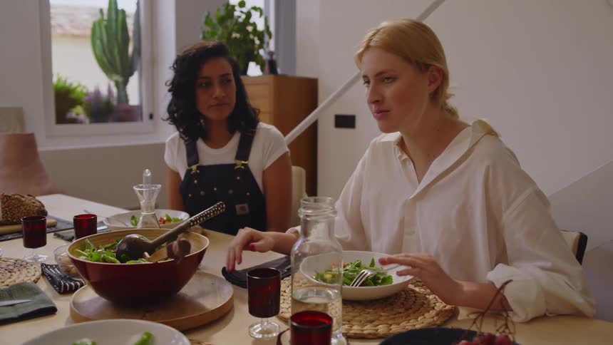 Three women and a man sitting at a table with food and drinks talking