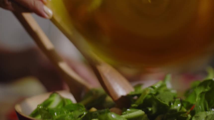 Person adds oil to a salad before tossing the salad