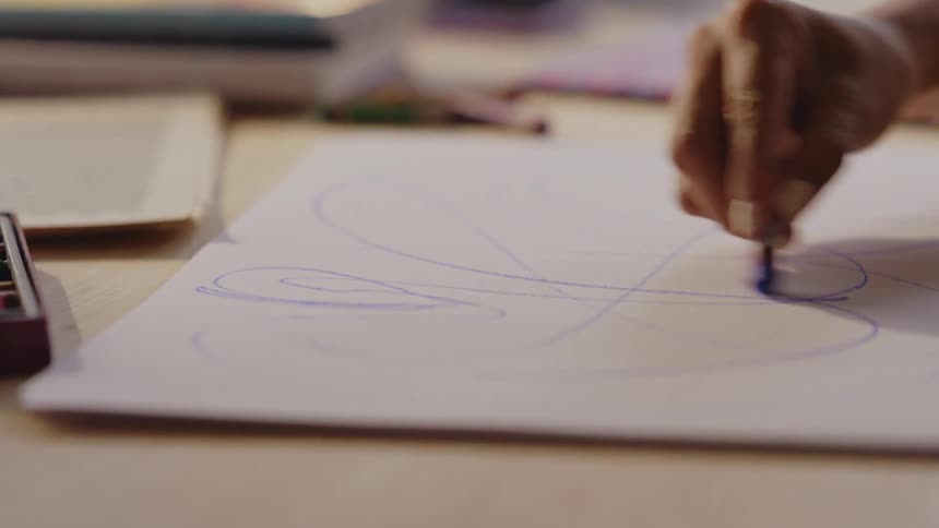 Hand holding blue crayon and drawing on white cardboard