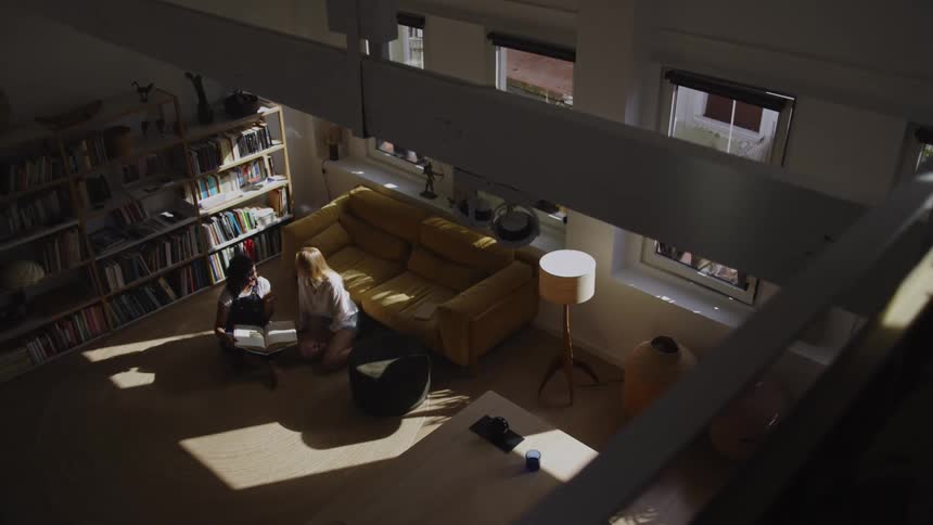 Top view of two women sitting on living room rug talking