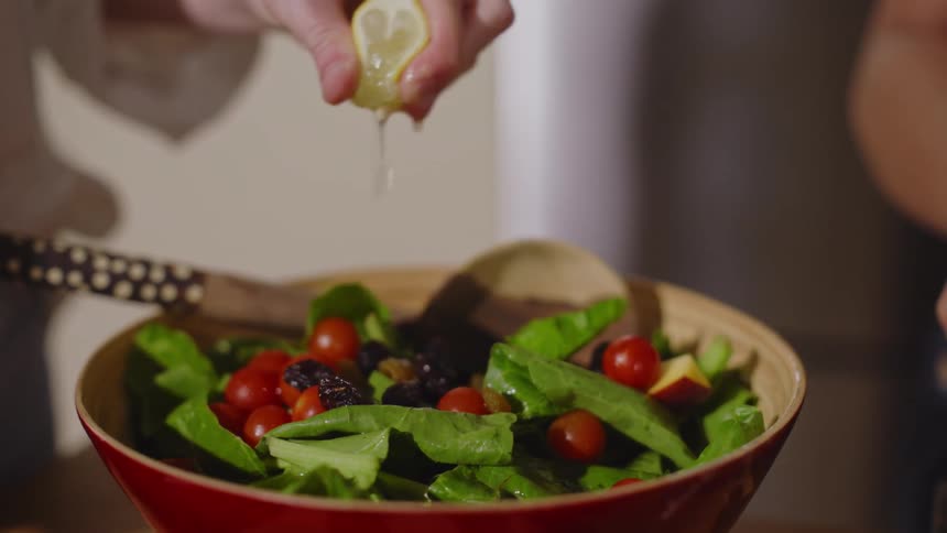 A hand squeezes lemon juice over a bowl of fresh salad