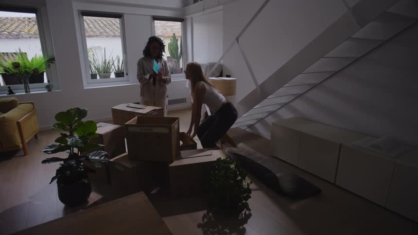 Two people unpack boxes and plants in a bright modern space with large windows