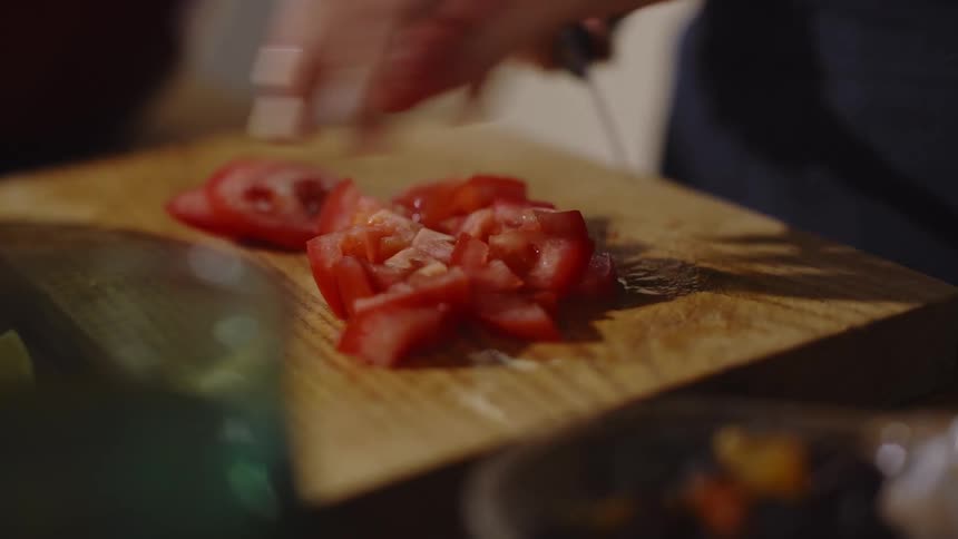 An adult chops fresh tomatoes on a wooden cutting board