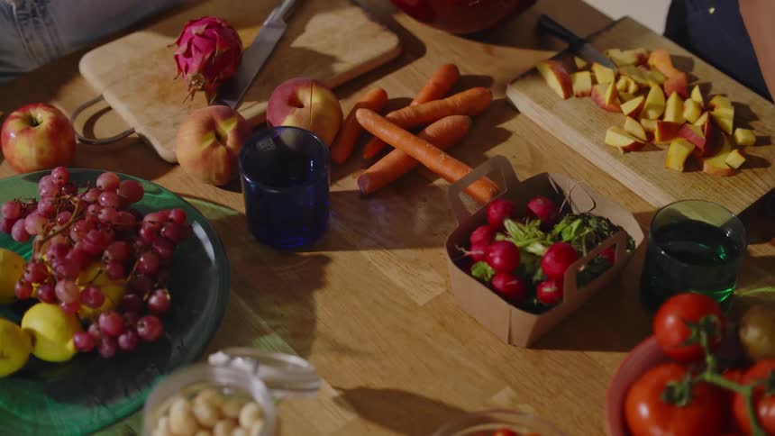 Two people are slicing fresh fruit and filling water glasses