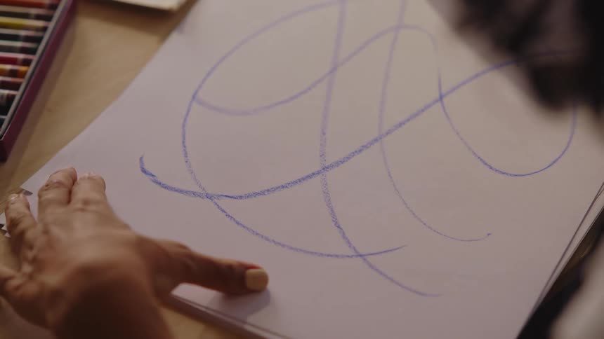 Woman sitting at a table draws with a blue pastel