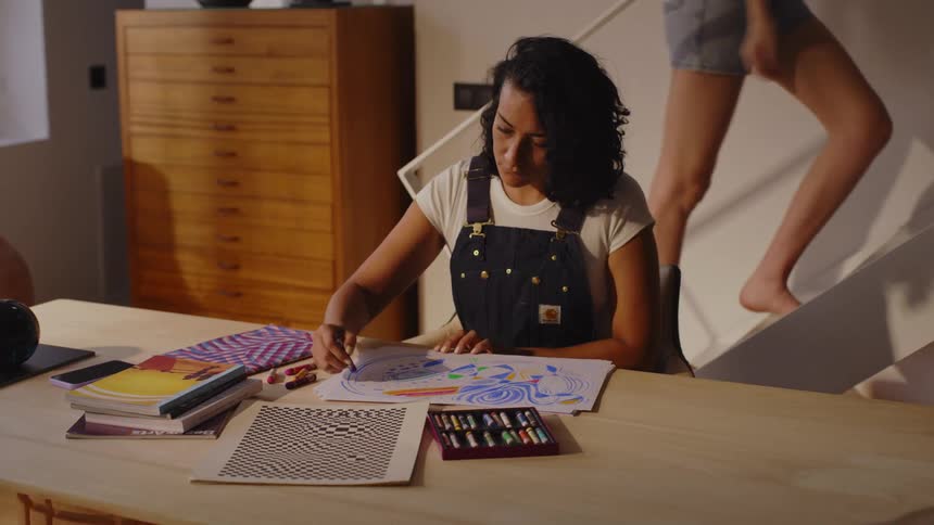 Woman drawing with crayons and in the background another woman walking up the stairs
