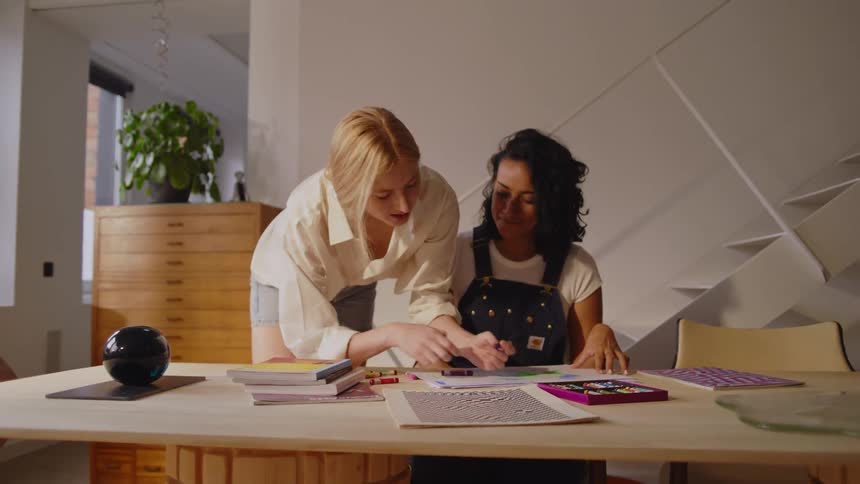 Two women use crayons to color on a piece of paper