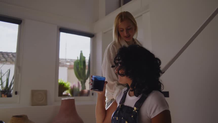 Woman sitting down drawing and another blonde woman leaving her a glass of water