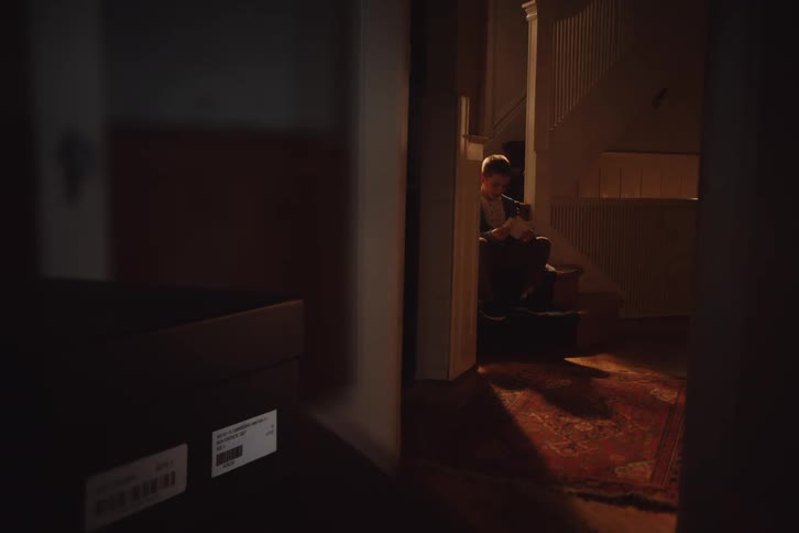 A child sits on a staircase in a dimly lit hallway reading something
