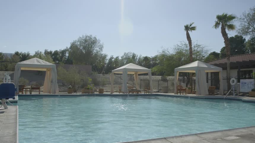 A pool is surrounded by chairs and cabanas on a bright sunny day
