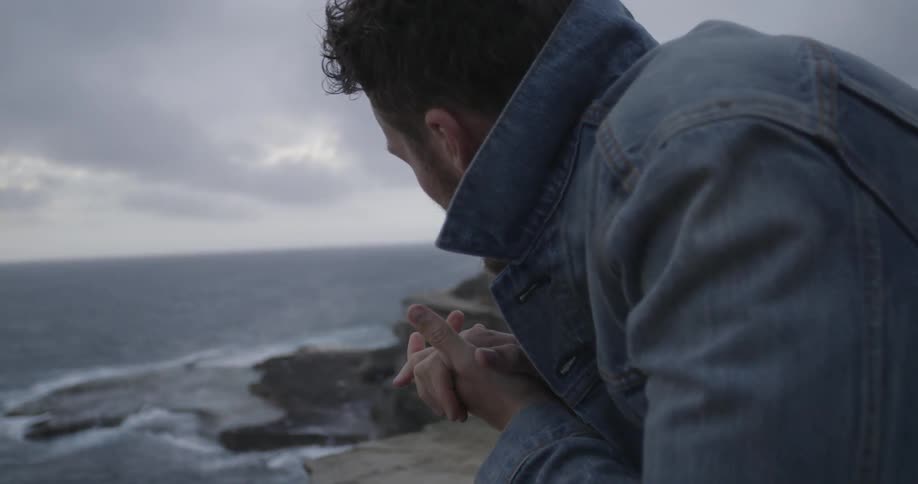 Man rubs his hands together on a cloudy day by the coast