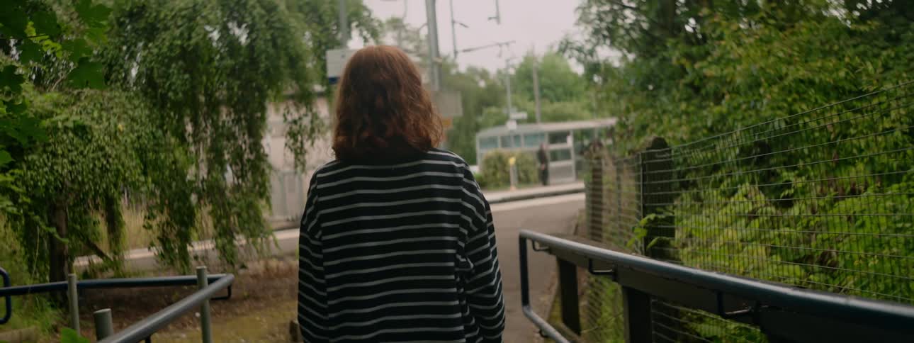 A person wearing a striped shirt walks down a path at a train station