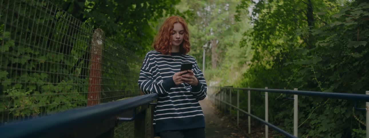 Redhaired woman using smartphone while standing in an environment surrounded by greenery