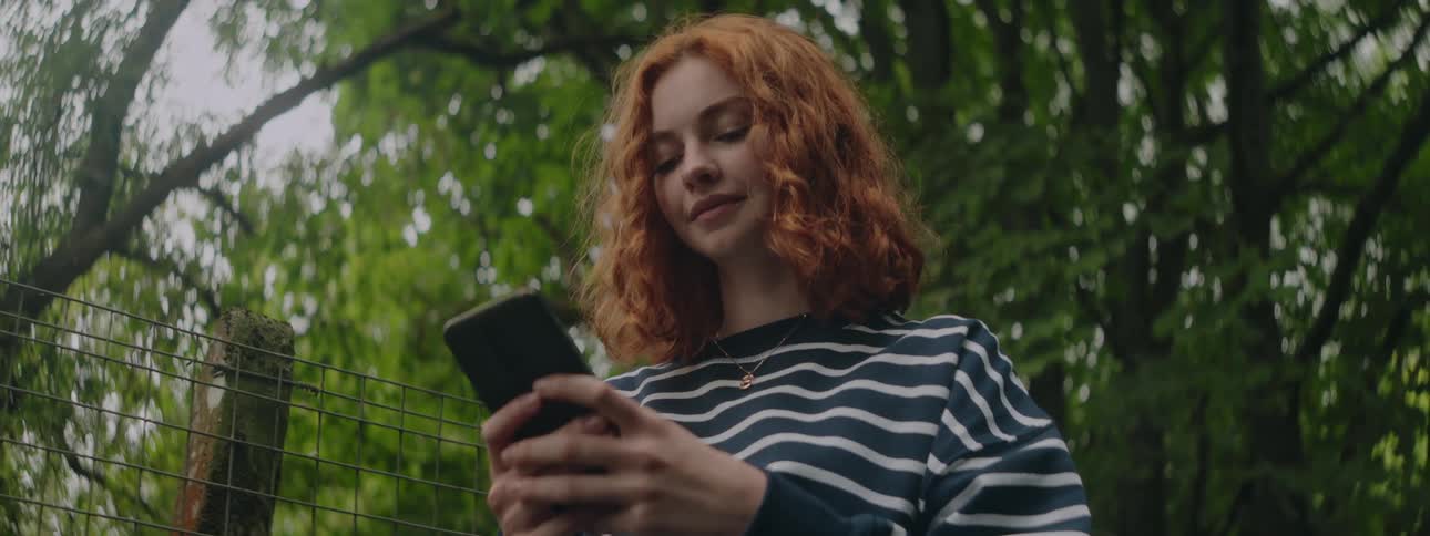 Woman in a park with trees using her smartphone