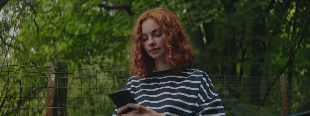 Redheaded woman using her cell phone in a natural environment surrounded by trees