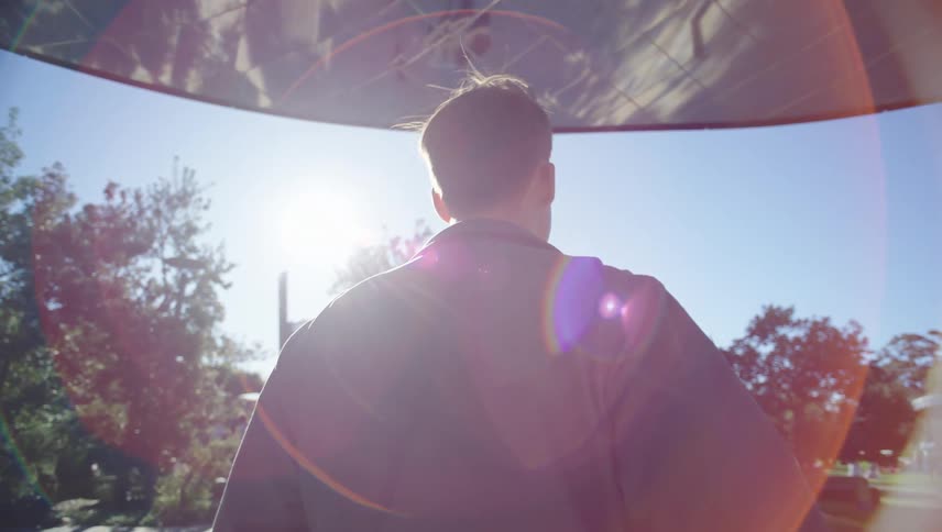 A person walks under a large reflective canopy with trees and a clear sky in the background