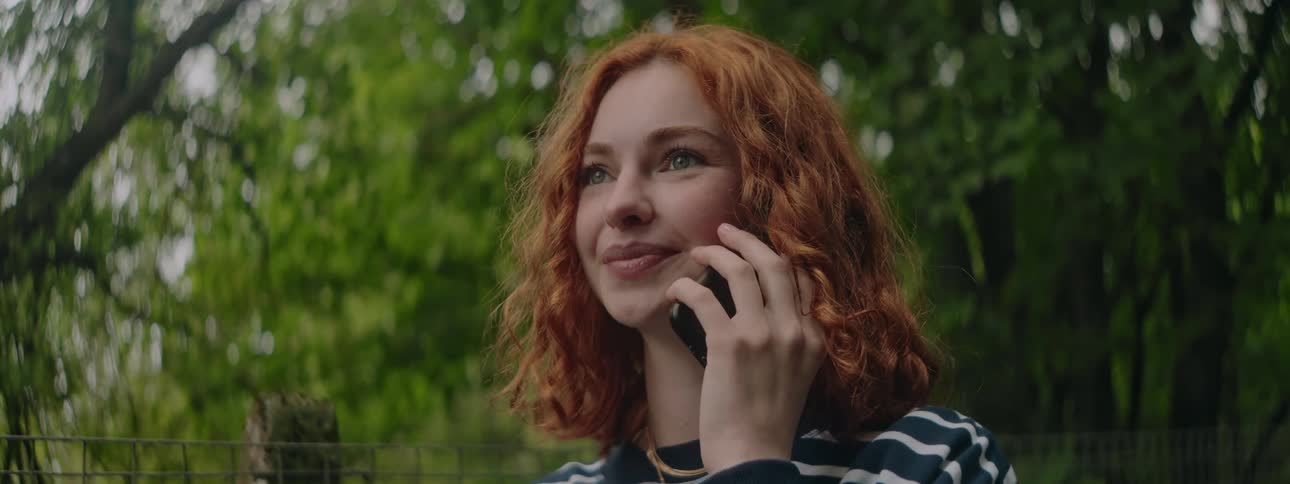 Cheerful redhead woman talking on a call on smartphone