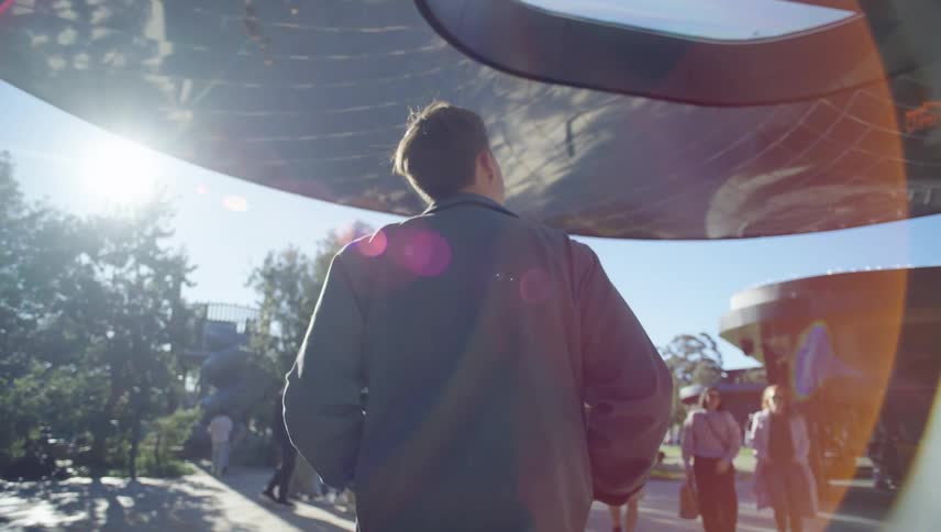 A person is walking under a large reflective curved roof leading to a park