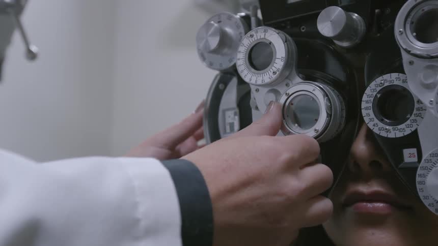 An optometrists is adjusting a phoropter as she checks a patient's eyes