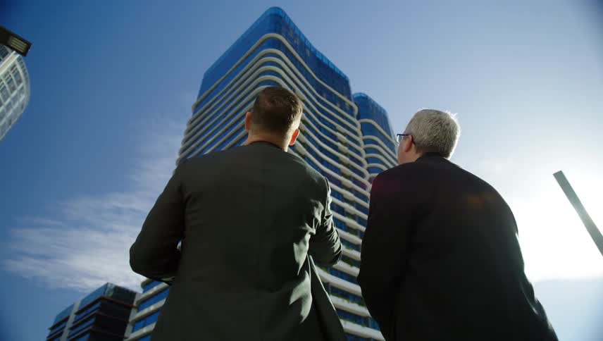 Two men talking while pointing at a modern building in a metropolis