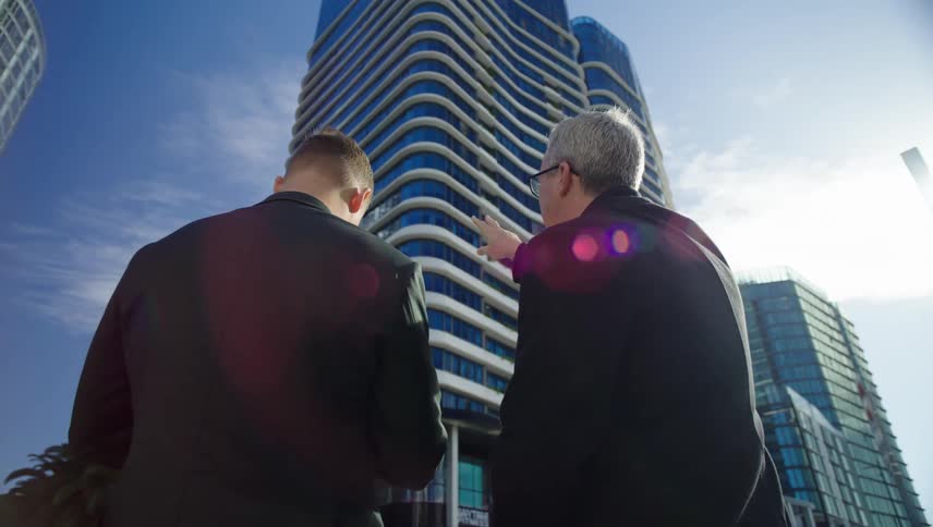 Two men talking while pointing and observing modern buildings in a metropolis during daytime