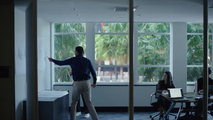 Four people in an office room talking and interacting with a project on a whiteboard