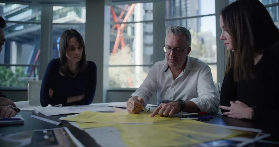 Man writing on a project on a table with people around him watching